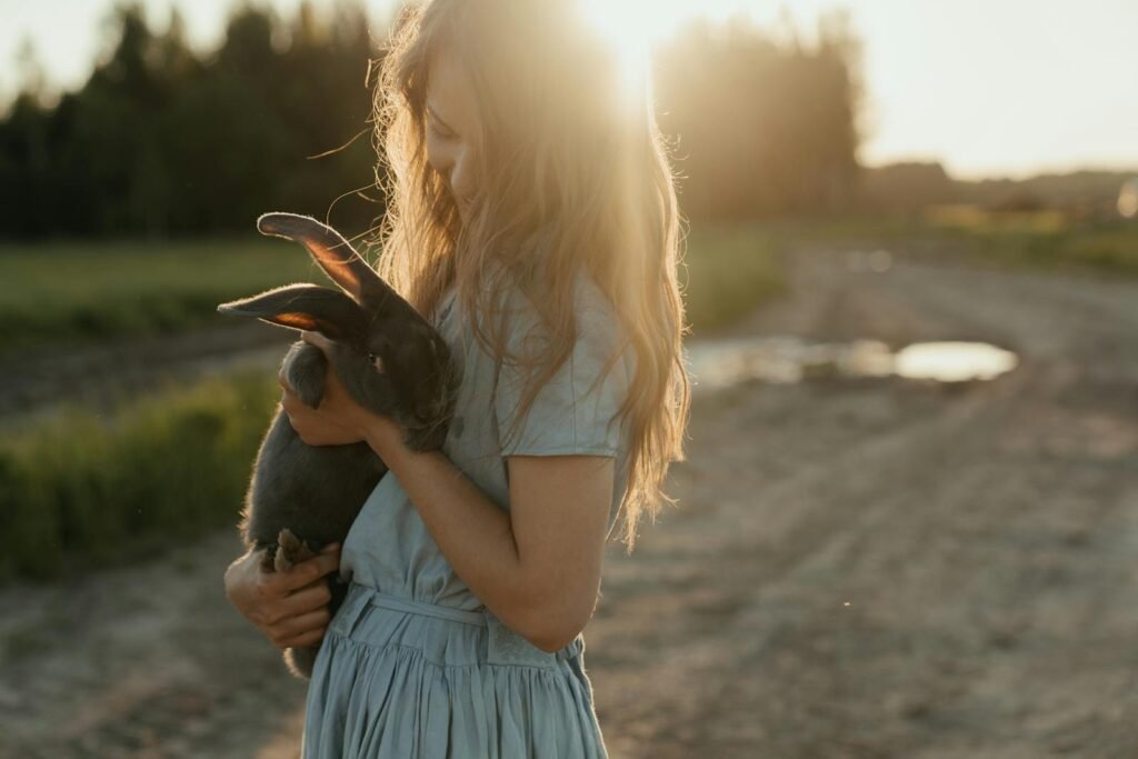 Urgencias Mascotas Lugo - A young girl lovingly holds a rabbit outdoors at sunset, surrounded by picturesque farmland.
